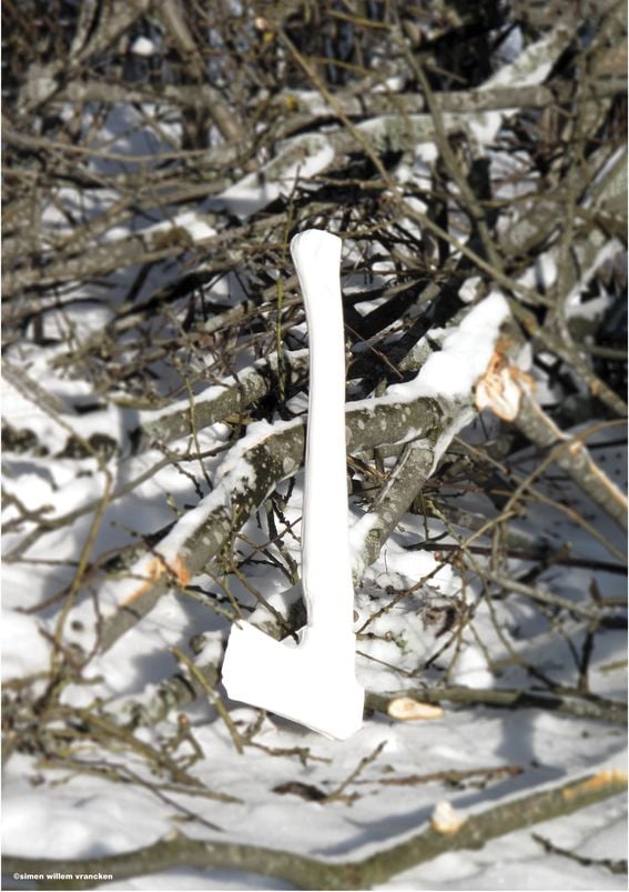 A white axe resting on a pile of branches and snow