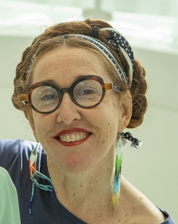 A cheerfully smiling woman with glasses looks straight into the camera, her hair braided around her head