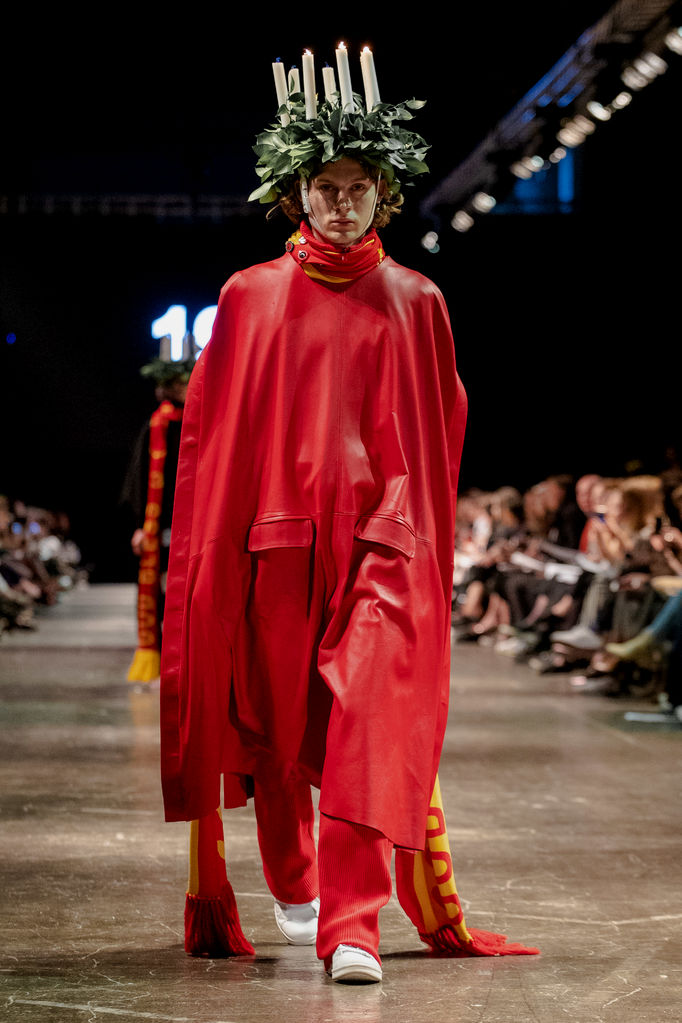 Model walking catwalk in red garment and headpiece with candles
