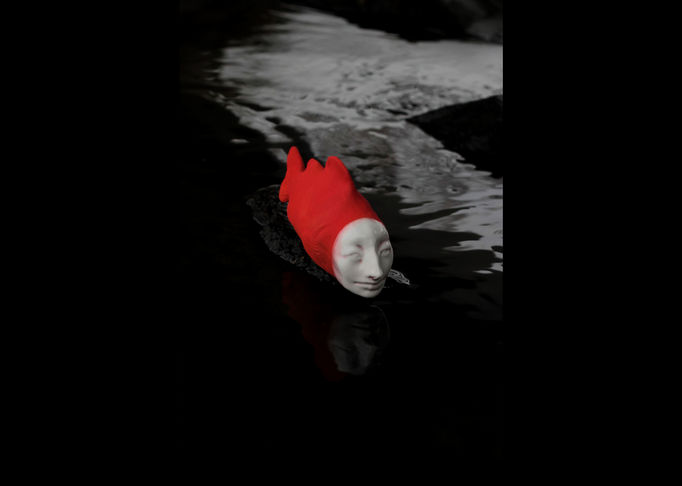 a ceramic fish with human-like face and red body with black background