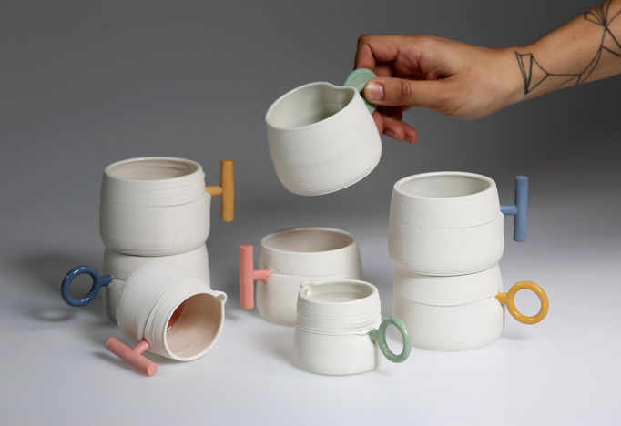 A set of colourful 3D printed clay cups and a hand holding one