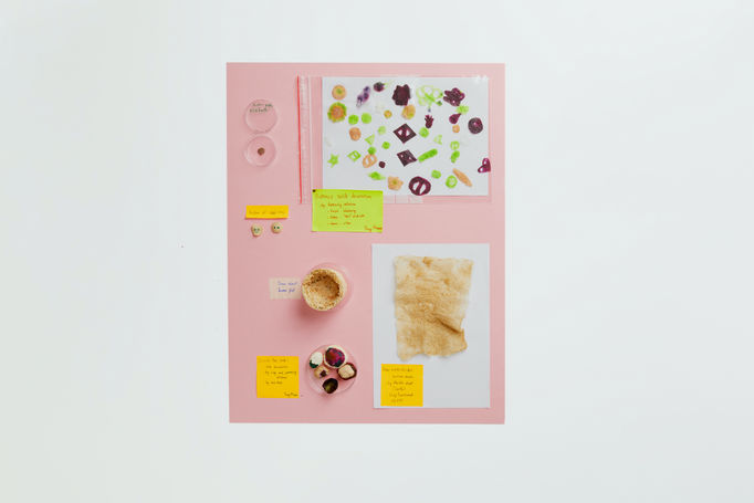 Portfolio photo of items produced while experimenting in the laboratories during the Aalto University Summer School course Nordic Biomaterials with CHEMARTS. The times are displayed on a light pink background and photographed from above. The items are different types of paper and items produced out of biomaterials such as beige buttons of dried MFC, a pot made of saw dust.