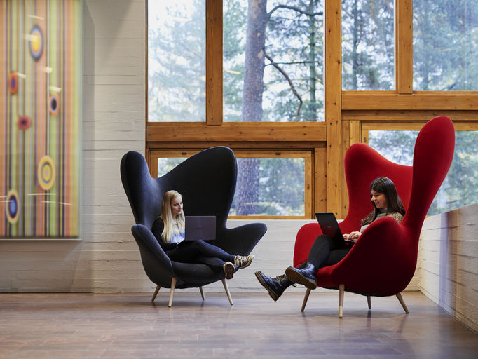 Two students are sitting in large, colourful chairs inside Dipoli