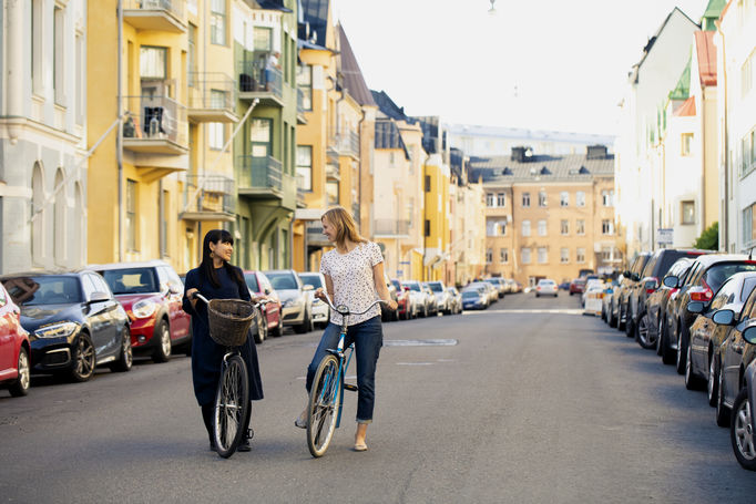 Two women on bikes surrounded by colourful house fasades on Huvilankatu in Ullanlinna neighbourhood, Helsinki.