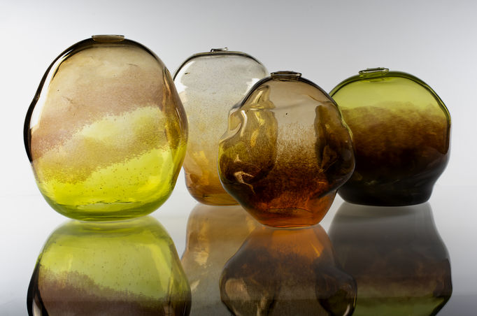 four nature-coloured glass objects with reflections underneath them