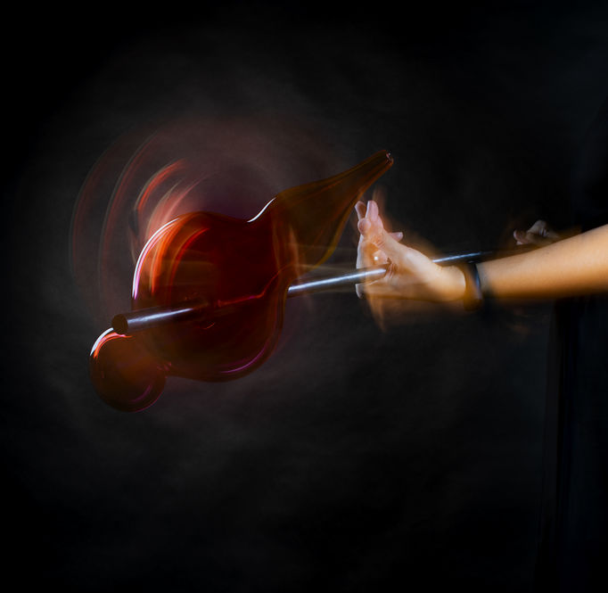 a person holding a glass blowing tool with a glass scultupre on it with dark background