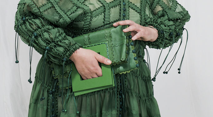 yksityiskohta asukokonaisuudesta, kuvassa vyötärön korkeudelta otos vihreästä mekosta ja mallin kädessä käsilaukku
