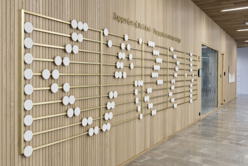 Kuvassa Kauppakorkeakoulun seinäteos: helmitaulu, johon on sijoitettu kauppatieteisiin lahjoittaneiden nimikoituja, valkoisia helmiä.
