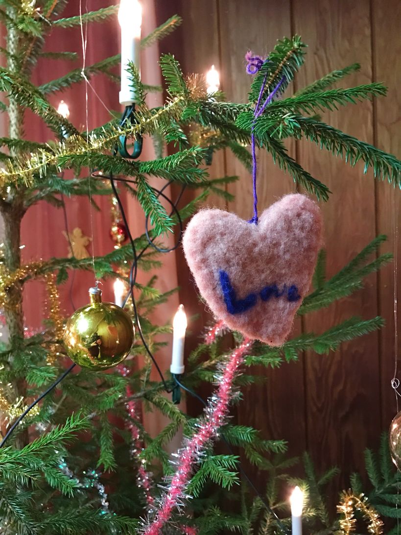 A self-made Christmas ornament on a Christmas tree: a felt heart that says love.