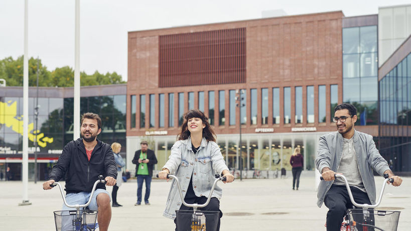 Kolme opiskelijaa pyöräilemässä kauppakeskus ABlocin edustalla
