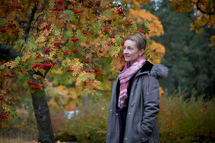 Johanna Kaipio seisoo ulkona, taustalla ruskan värittämä pihlajapuu ja pensaita.