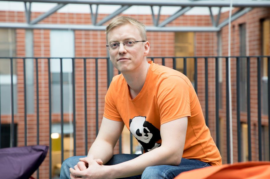 Jara Uitto sitting at Computer Science building, looking at the camera and wearing an orange t-shirt with a panda on it