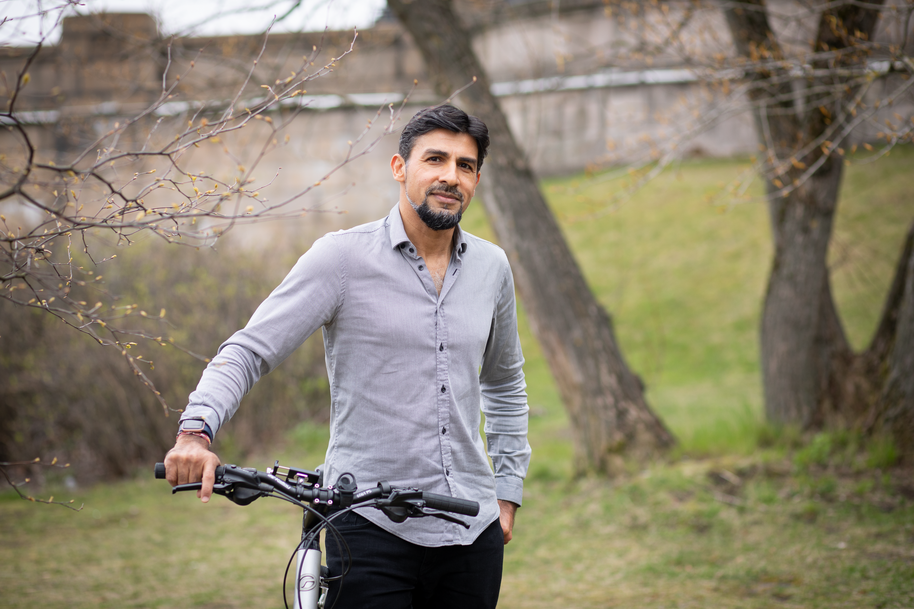 Nitin Sawhney standing outdoors with his bike, green grass and trees on the background