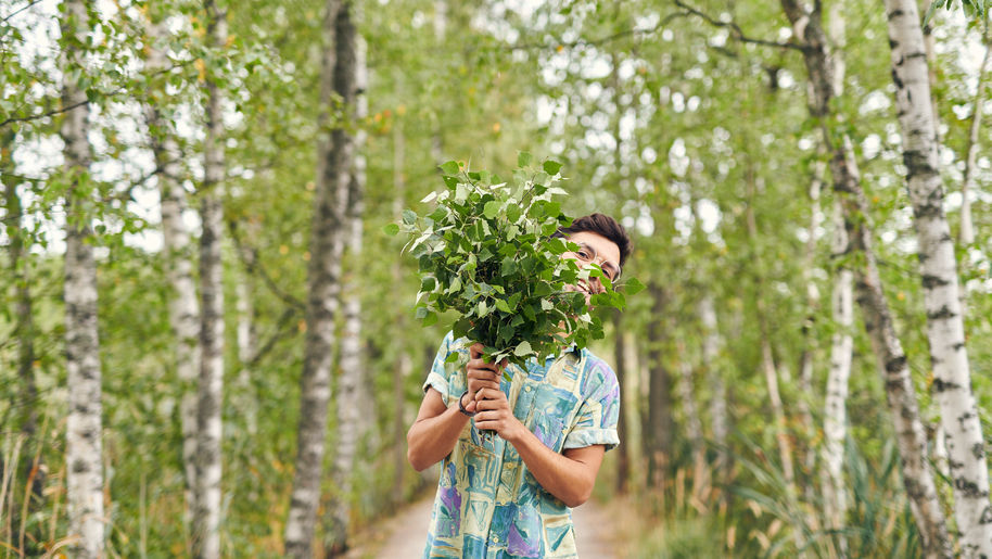 A guy peeks from behind fresh green birch branches. Photo: Aalto University / Unto Rautio
