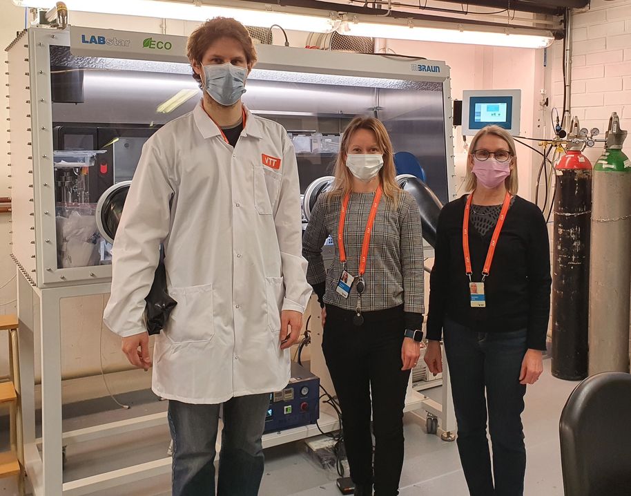 A man wearing a lab coat and two women, all wearing face masks, in front of an argon glove box.