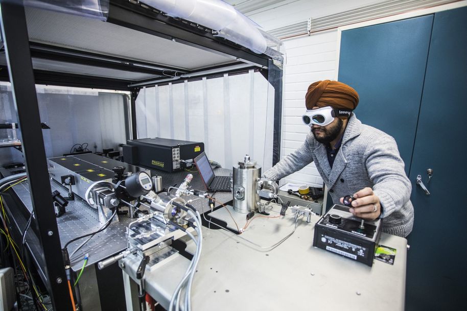 A man wearing protective glasses working on laser ablation in a pressurized chamber.