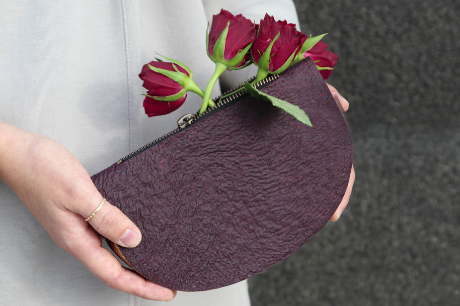 Photo by Irene Purasachit. Person holding a burgundy coloured clutch purse in two hands, red roses are seen coming out of the zipper at the top