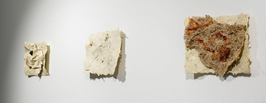 three paper like sculptures hung on a white wall