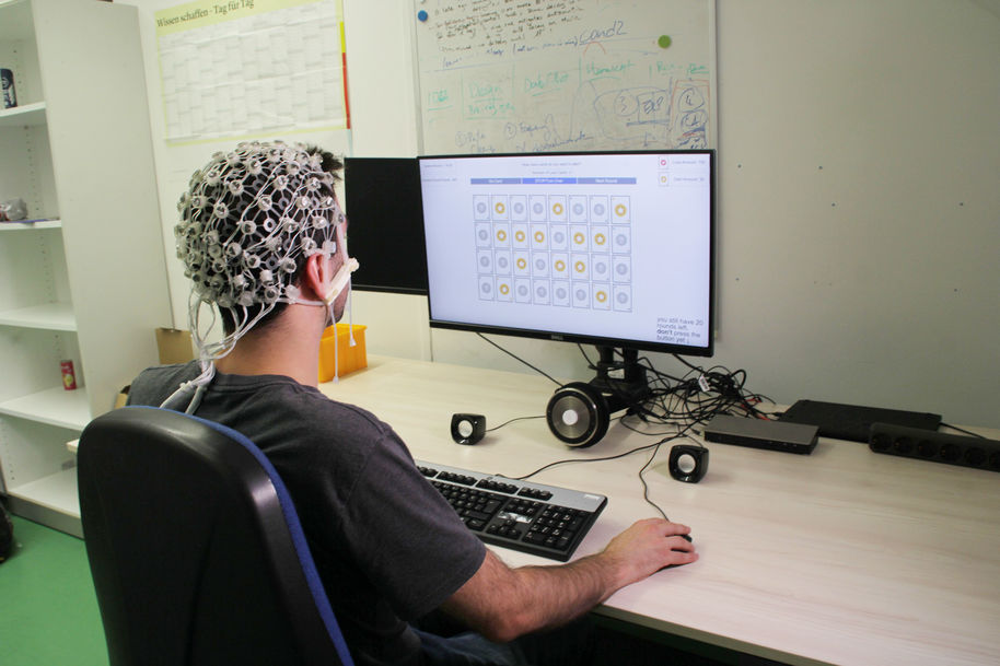 Male participant in psychological study with sensors attached to his head clicking through an experiment on a computer in a white office space