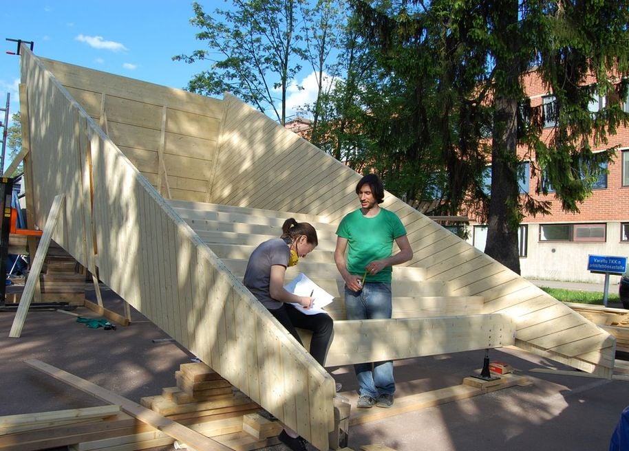 Two people working on with a wooden structure outdoors in summertime