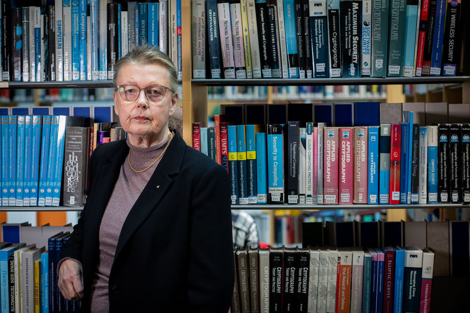 Professori Kaisa Nyberg seisoo kirjahyllyn edessä Aalto-yliopiston tietotekniikan talossa