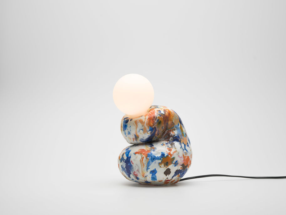 A colourful organically shaped lamp, its body folding in on itself while a sphere light shade is sitting on top
