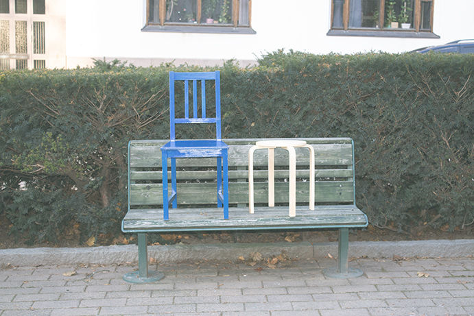 A blue chair and wooden stool ”sitting” on a bench