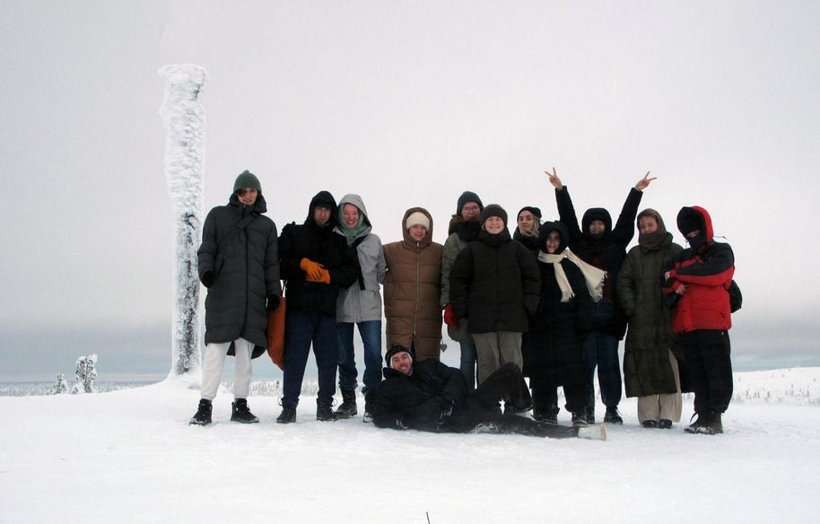 A group of people in thick jackets taking a picture in during a snowy white winter