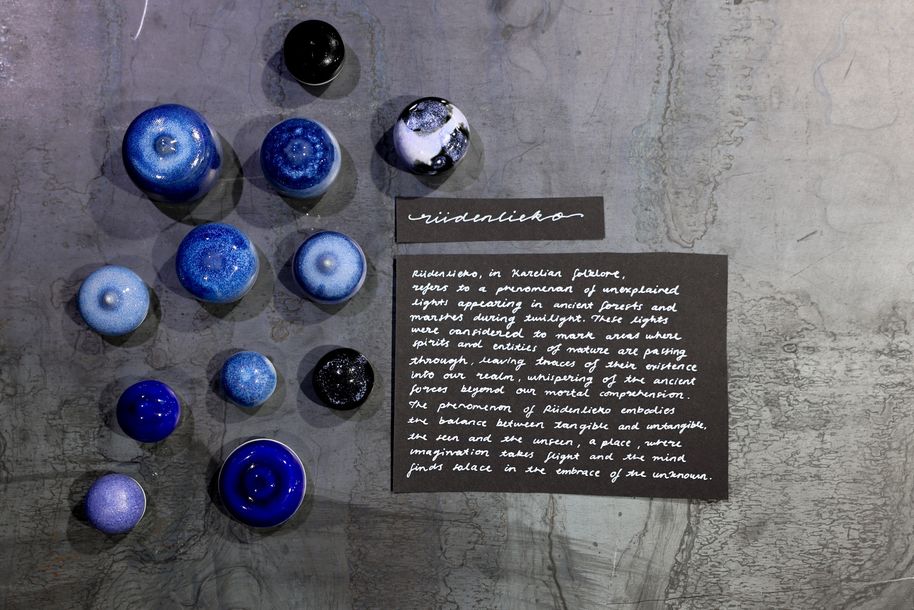 A collection of bulbous, blu ceramic objects accompanied by a handwritten text on a black paper on the right