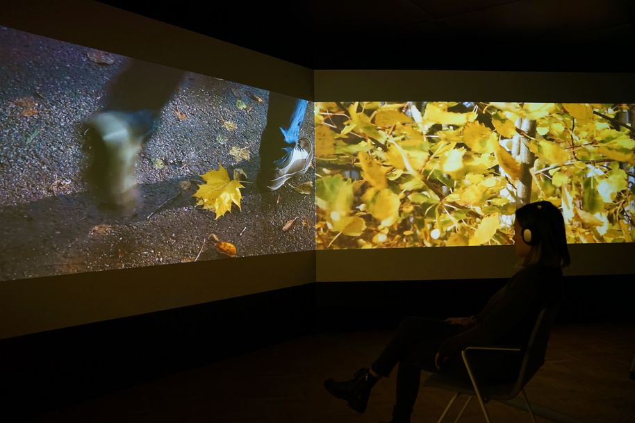 Three screen forming a long immersive video experience, a pair of feet on the left screen and yellow leaves on the right screen