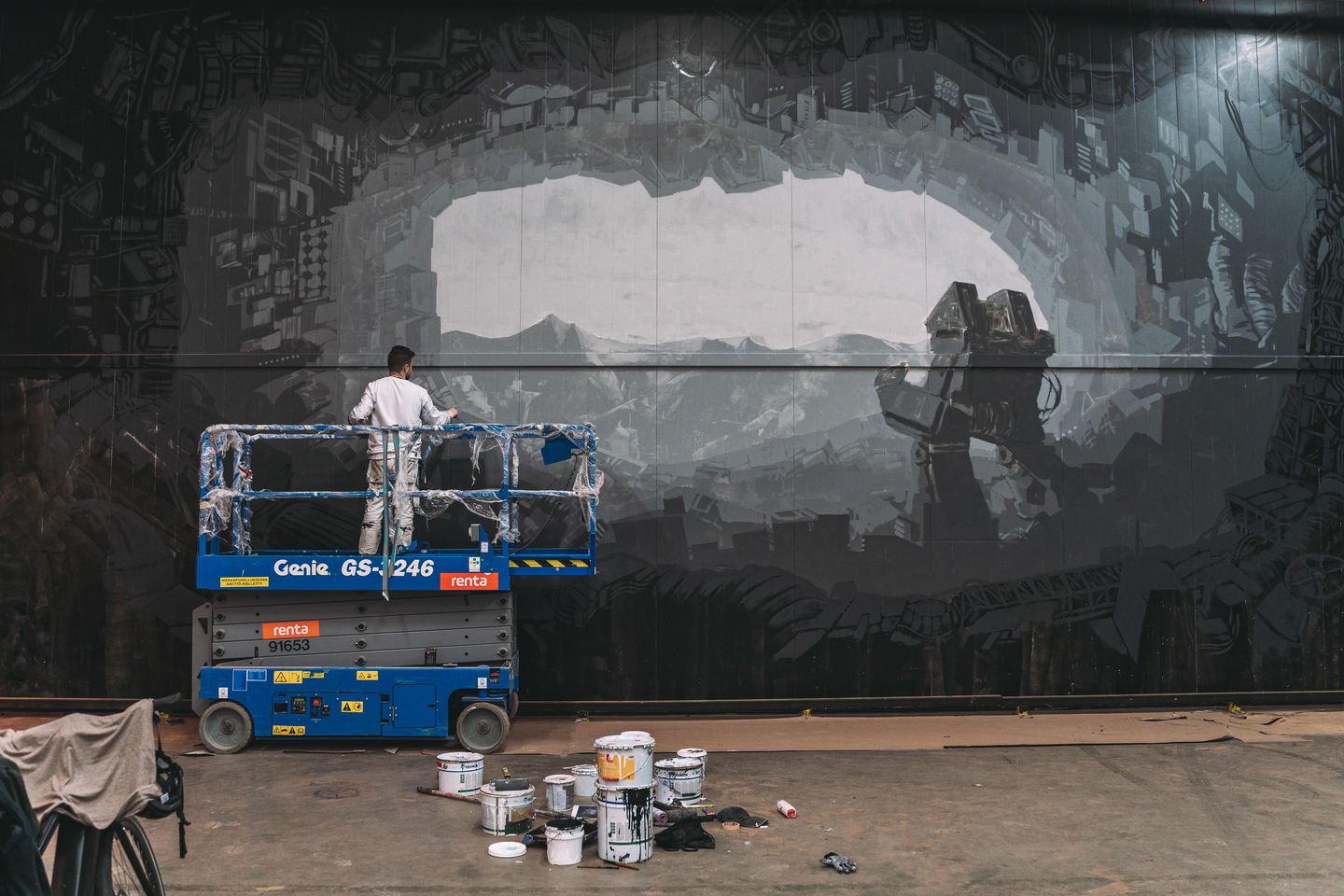 Artist Jesse stands on a scissor lift to paint the greyscale mural in Keran Hallit
