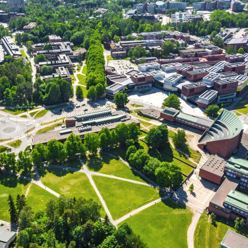 Aerial view of the campus in summer, Undergraduate Centre, Learning Centre, Väre, A Bloc and School of Business in view on a sunny day. Grass and trees are vibrant and green.