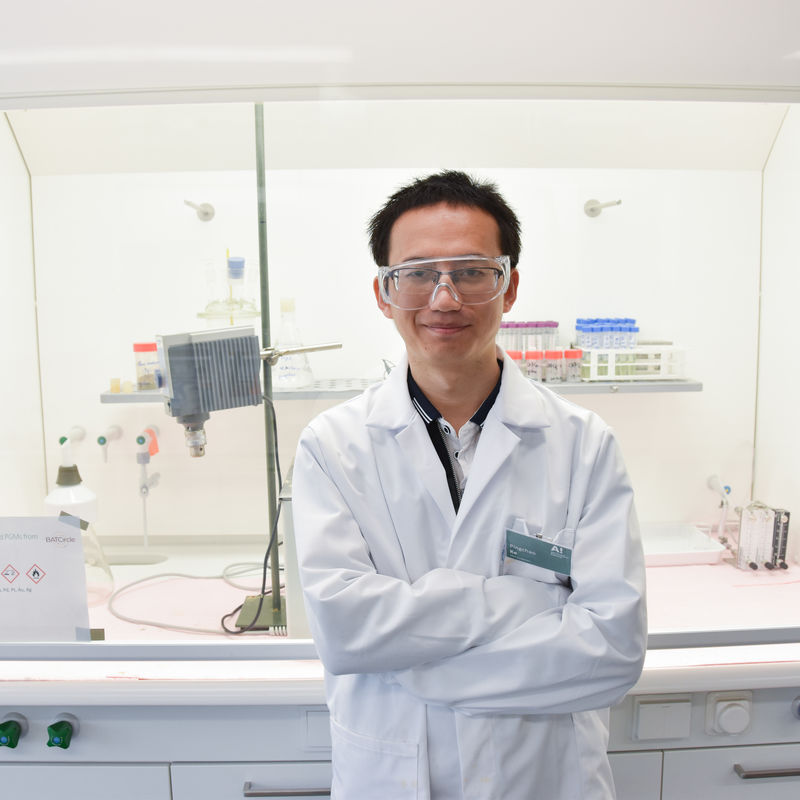 Pingchao Ke in the laboratory with safety gear standing in front of lab equipment smiling